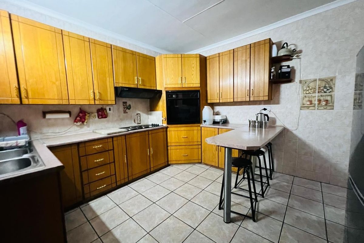 A functional kitchen featuring wooden cabinetry, laminate countertops, a built-in oven, hob, extractor fan, and a breakfast bar with tiled flooring.