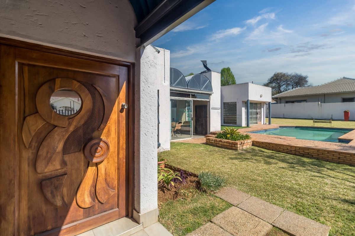 Rear exterior view featuring a swimming pool, brick landscaping, and a unique carved wooden entrance door leading into the home.