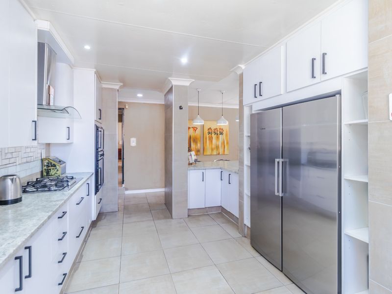 Modern kitchen featuring white cabinetry, stone countertops, gas hob, built-in oven, and tiled flooring with a clean, functional layout.