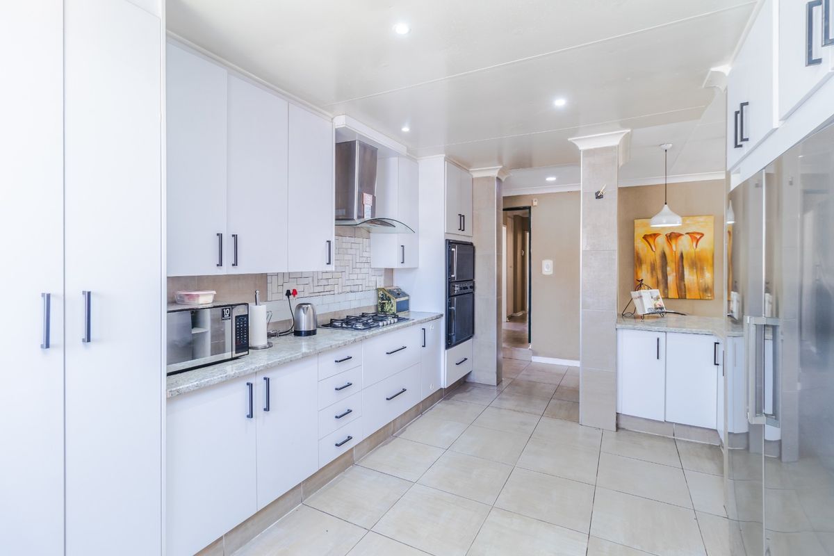 Modern kitchen featuring white cabinetry, stone countertops, gas hob, built-in oven, and tiled flooring with a clean, functional layout.
