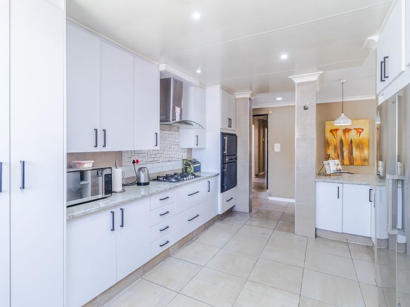 Modern kitchen featuring white cabinetry, stone countertops, gas hob, built-in oven, and tiled flooring with a clean, functional layout.
