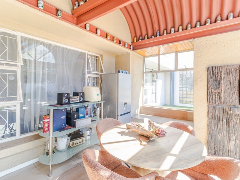 A sunlit enclosed patio area featuring a distinctive vaulted corrugated metal ceiling, steel beams, and large windows providing ample natural light.