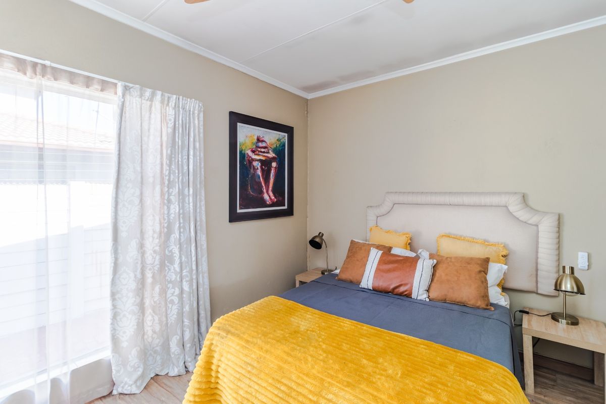 A well-maintained bedroom featuring neutral wall tones, laminate flooring, and a sliding door providing natural light.