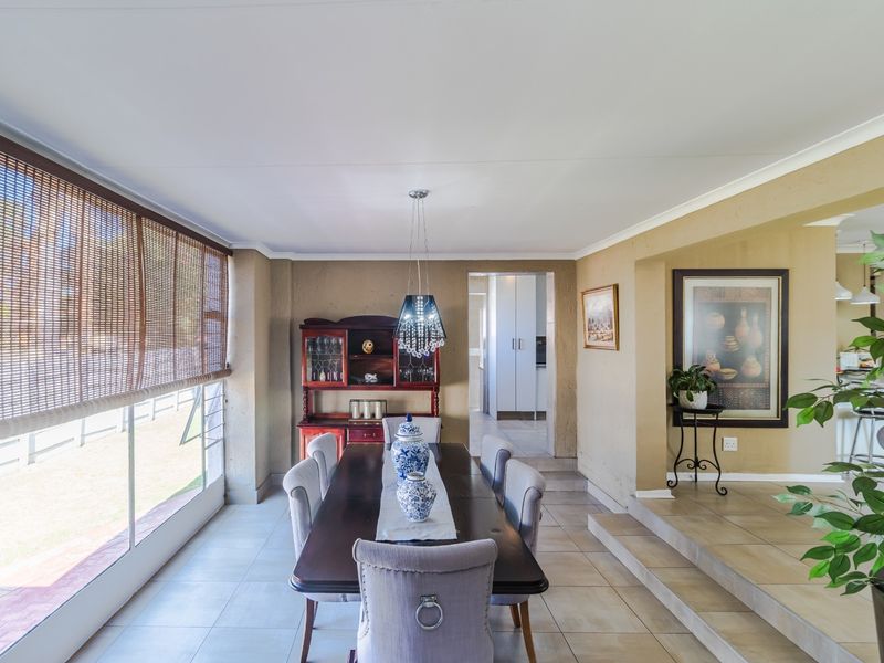 Spacious dining room featuring tiled flooring, large windows with bamboo blinds, and a raised floor transition leading to an adjacent living area.