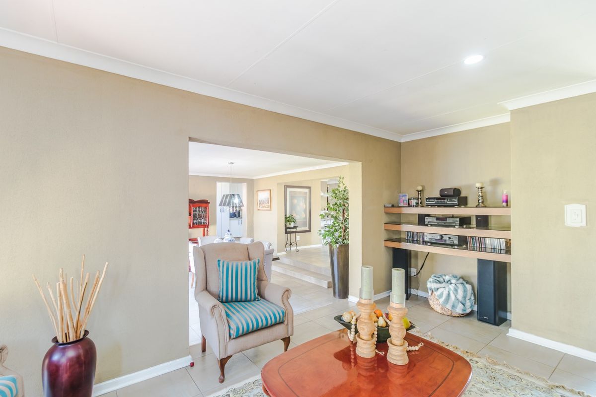 A well-maintained living room featuring tiled flooring, built-in shelving, and a coved ceiling, with an open-plan flow into the adjacent dining area.
