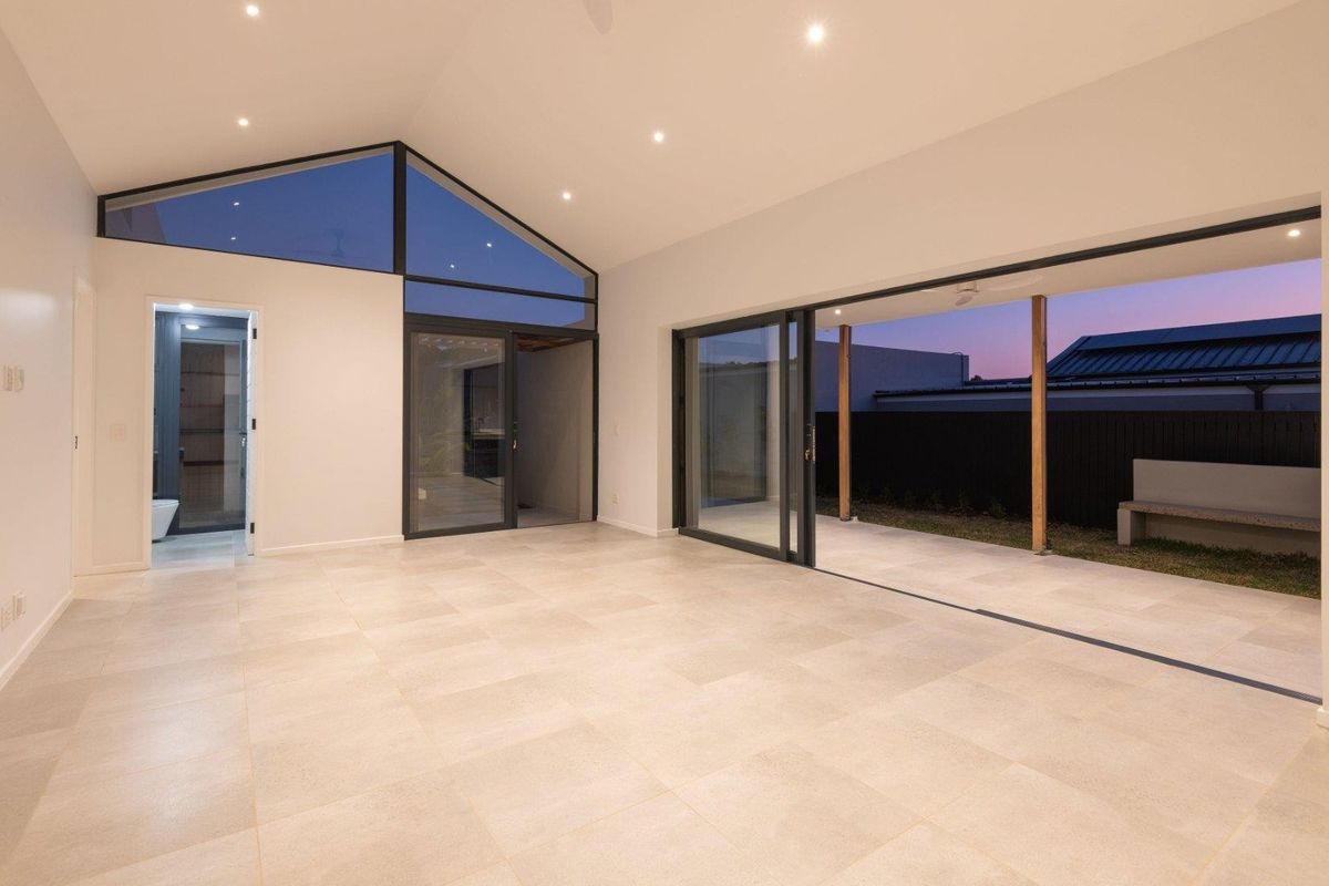 Spacious, modern open-plan living area featuring vaulted ceilings, large sliding glass doors opening to a covered patio, and neutral tiled flooring.