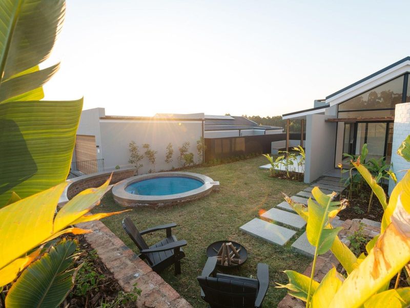 A well-maintained rear garden featuring a circular plunge pool, paved stone pathway, and brick retaining wall, set against a modern residential structure.
