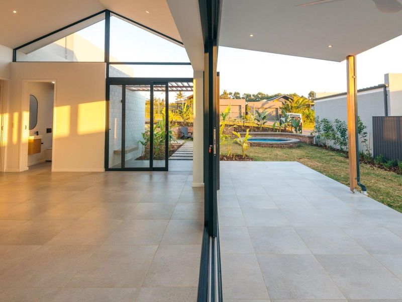 Modern open-plan living area featuring large format tiles, vaulted ceilings, and seamless indoor-outdoor flow to a covered patio and garden area.