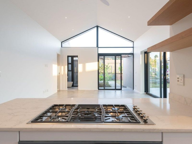 Modern open-plan kitchen and living area featuring a vaulted ceiling, high-end gas cooktop, built-in oven, and seamless access to the outdoor patio through sliding doors.