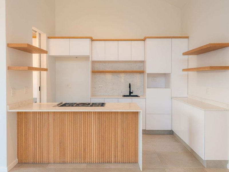 Modern kitchen featuring white cabinetry, timber slatted island, stone countertops, floating shelves, and a built-in gas hob in a bright, open-plan space.
