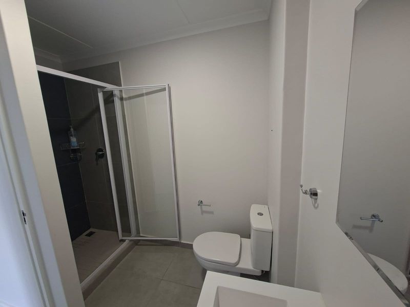 A clean, modern bathroom featuring a glass-enclosed shower, a white toilet, and a vanity basin with a wall-mounted mirror.