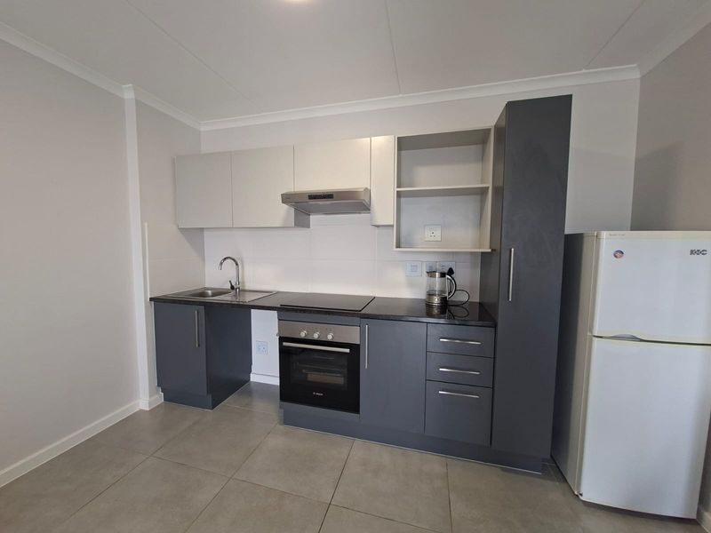 A modern, compact kitchen featuring two-tone cabinetry, built-in oven and hob, extractor fan, and neutral tiled flooring.