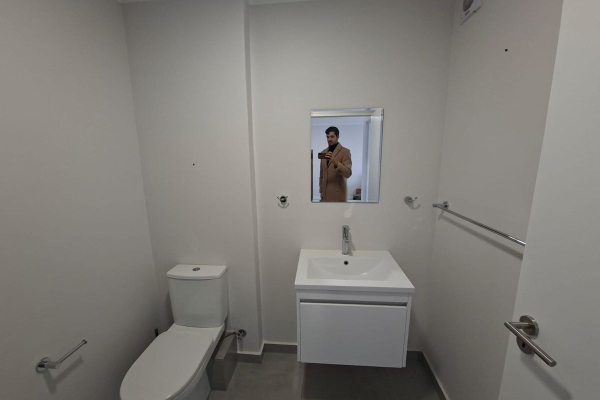 A clean, modern bathroom featuring a wall-mounted vanity with a basin, a toilet, and chrome fixtures, finished with neutral wall paint and floor tiles.