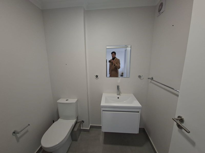 A clean, modern bathroom featuring a wall-mounted vanity with a basin, a toilet, and chrome fixtures, finished with neutral wall paint and floor tiles.