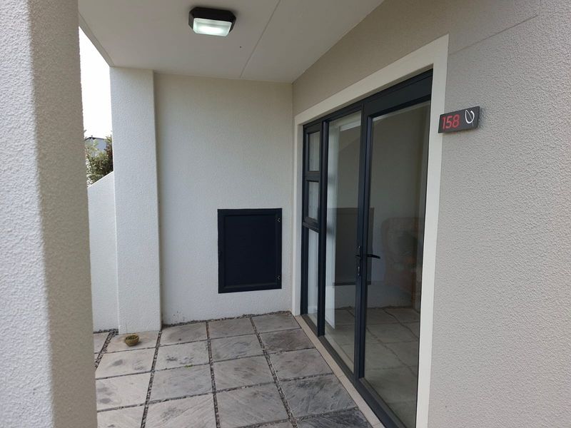 A clean and modern apartment entrance featuring stone tile flooring, a dark-framed sliding glass door, and unit number signage.