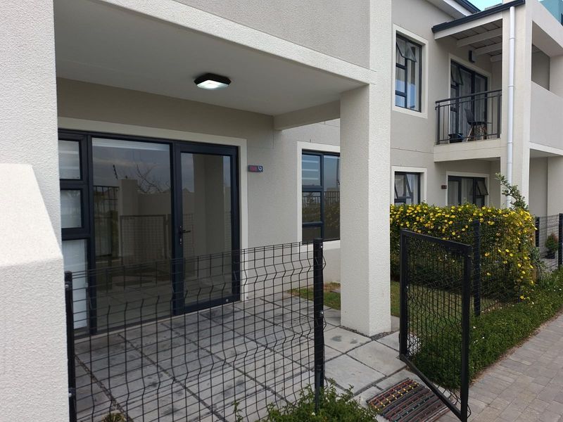 Ground floor apartment entrance featuring a paved patio area, secure wire mesh fencing, and modern aluminium-framed sliding glass doors.
