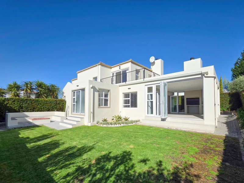 Rear view of a modern house featuring a landscaped garden, paved patio area with a built-in fire pit, and an open-plan indoor-outdoor living space.