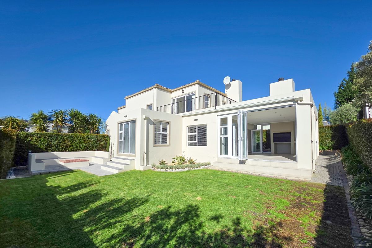 Rear view of a modern house featuring a landscaped garden, paved patio area with a built-in fire pit, and an open-plan indoor-outdoor living space.