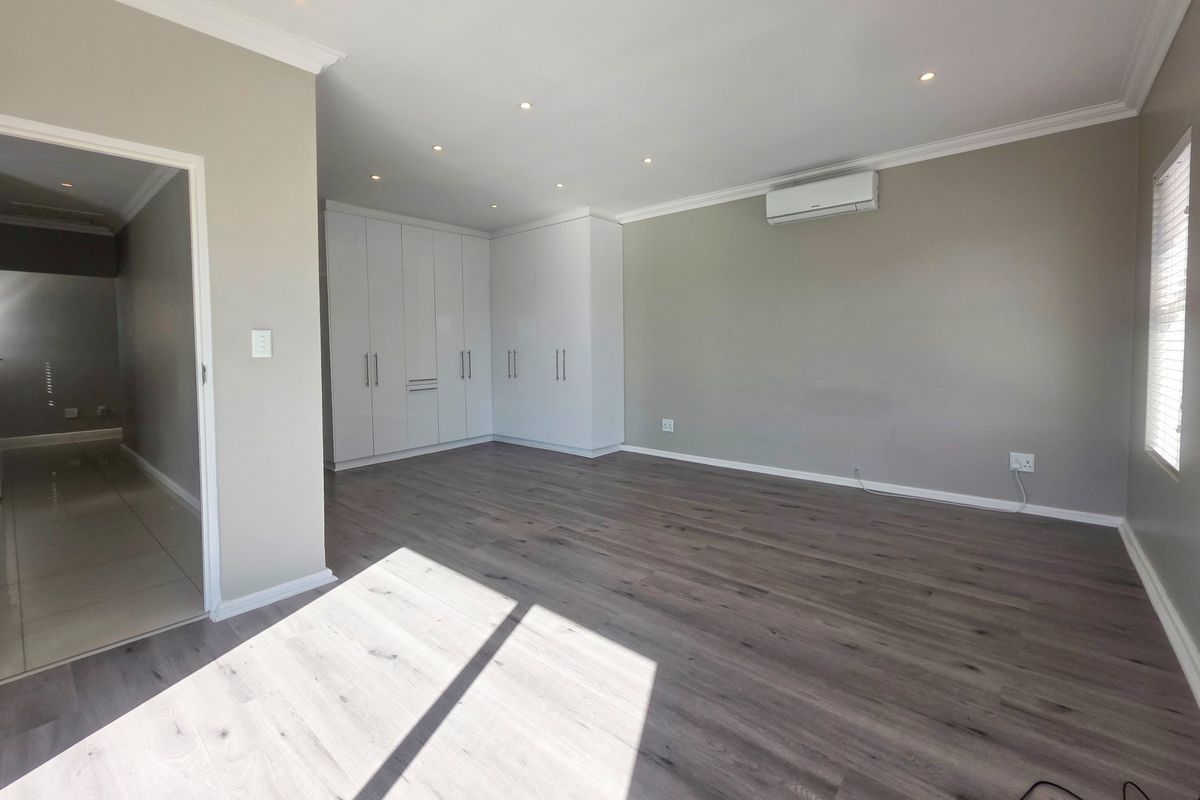 Spacious bedroom featuring modern laminate flooring, built-in cupboards, recessed lighting, and a wall-mounted air conditioning unit.