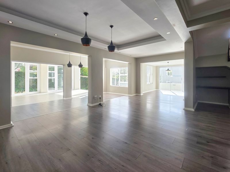 Spacious open-plan living area featuring modern laminate flooring, recessed ceiling details, pendant lighting, and large sliding doors providing ample natural light.