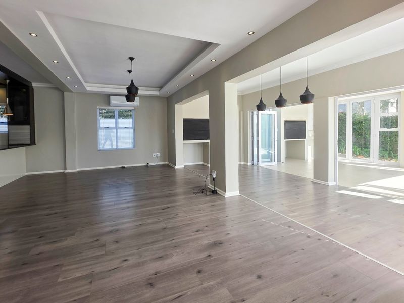 Spacious open-plan living area featuring modern laminate flooring, a tray ceiling with recessed lighting, and seamless access to the outdoor patio through sliding doors.