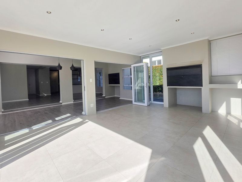 Spacious covered patio featuring tiled flooring, recessed lighting, and a built-in braai, with seamless access to the interior living areas through bi-fold doors.
