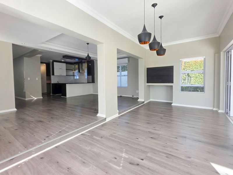 Spacious open-plan living and kitchen area featuring modern laminate flooring, neutral walls, recessed lighting, and seamless flow to the outdoor patio.