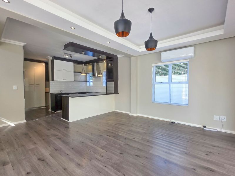 Spacious open-plan living area featuring modern laminate flooring, recessed lighting, a split-system air conditioner, and a contemporary kitchen with built-in cabinetry.