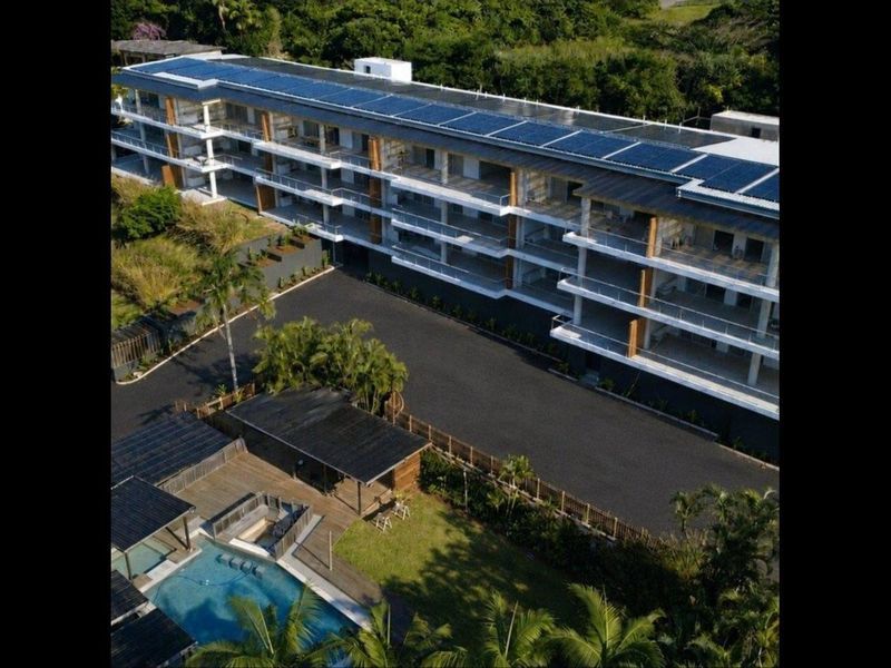 Aerial view of a modern apartment complex featuring solar panels, private balconies, a swimming pool, and landscaped grounds.