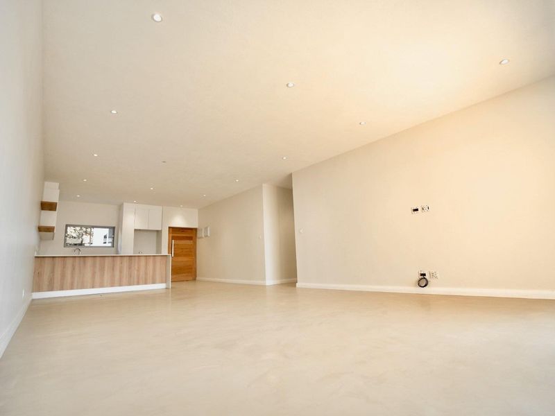 Spacious open-plan living area featuring polished concrete floors, recessed downlights, and a modern kitchen with integrated cabinetry and island.