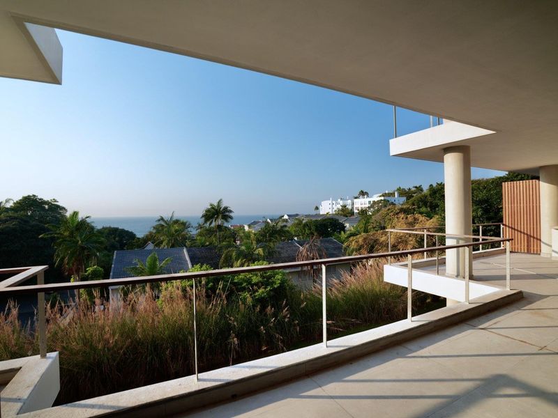 Spacious covered balcony featuring tiled flooring, a modern metal railing, and expansive views of the surrounding landscape and ocean.