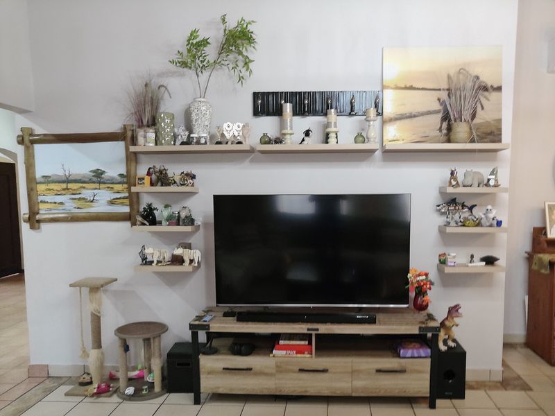 A living room featuring a wall-mounted television setup with multiple floating shelves and tiled flooring.