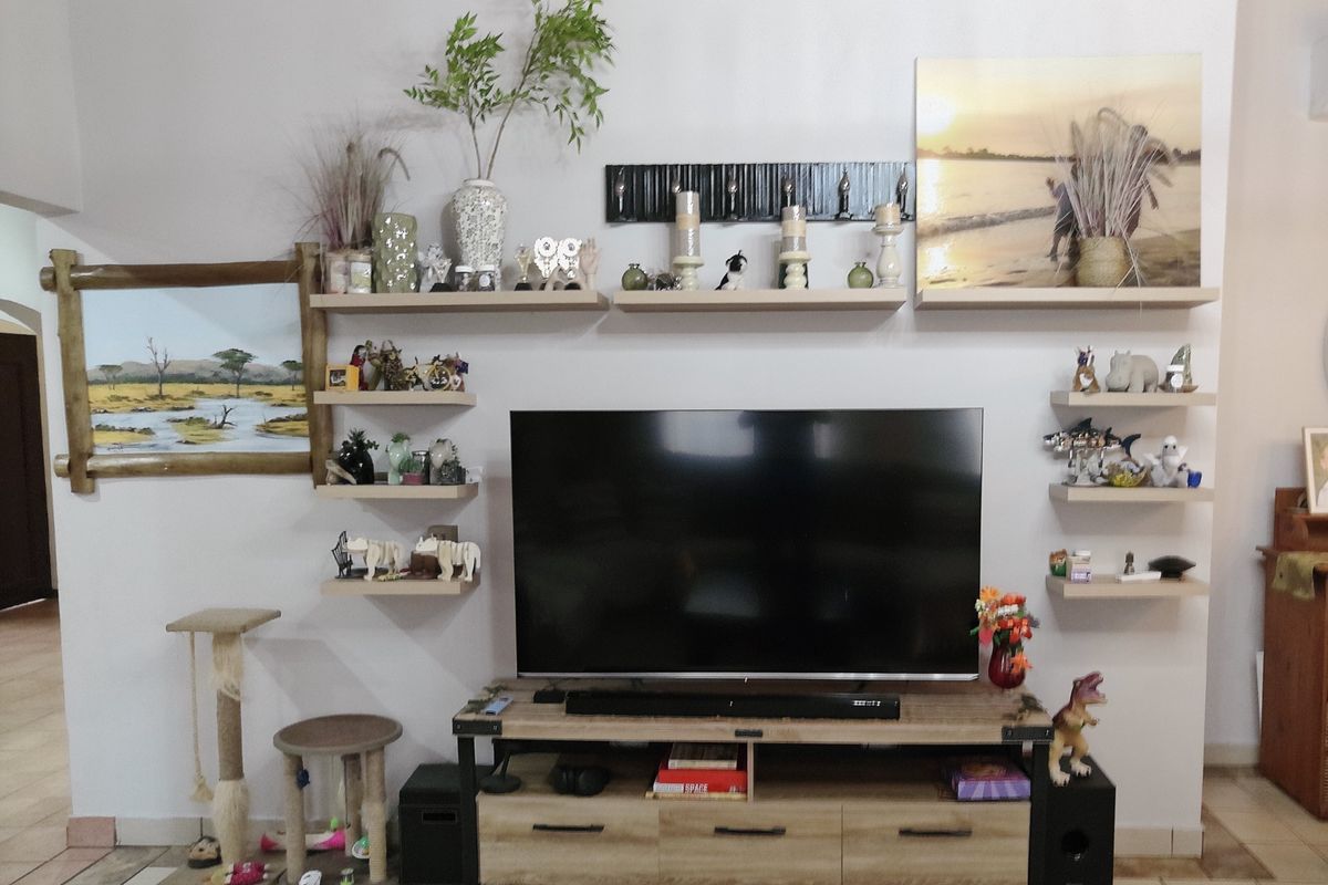 A living room featuring a wall-mounted television setup with multiple floating shelves and tiled flooring.