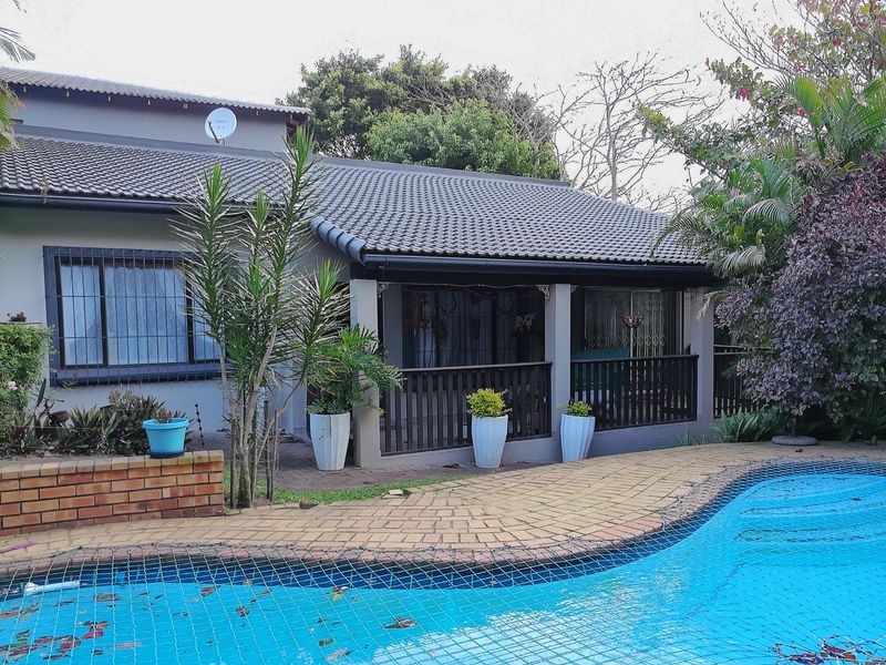 Rear exterior view featuring a swimming pool with safety net, paved surround, and a covered patio area with timber balustrade.