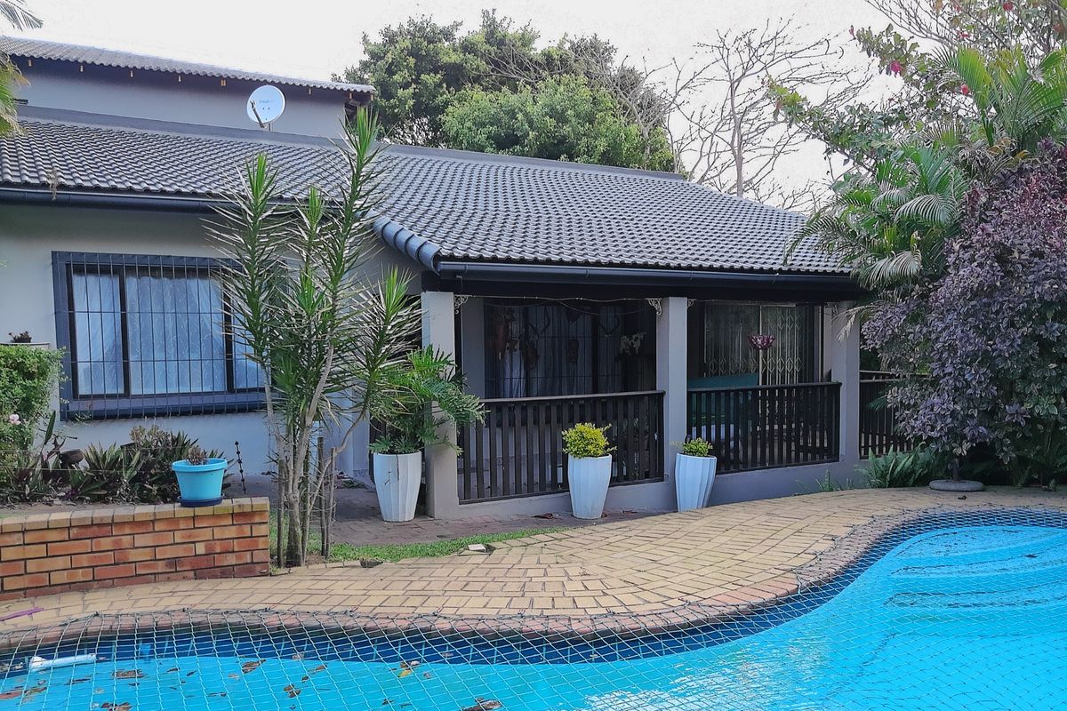 Rear exterior view featuring a swimming pool with safety net, paved surround, and a covered patio area with timber balustrade.