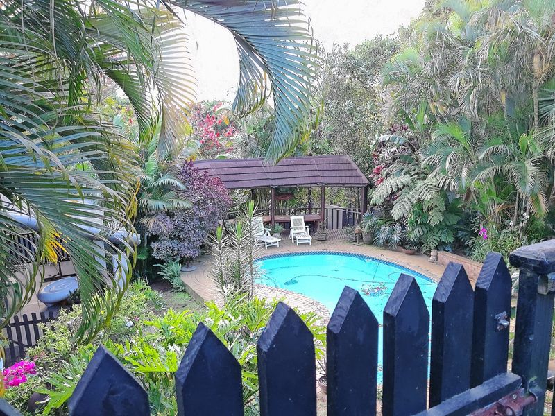 A lush garden setting featuring a swimming pool and a wooden gazebo, enclosed by a timber picket fence.
