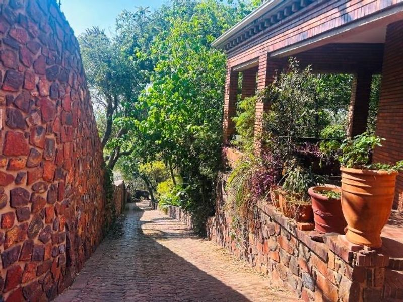 A charming exterior view featuring a stone-clad wall, brick-paved driveway, and a covered porch area with brick pillars.