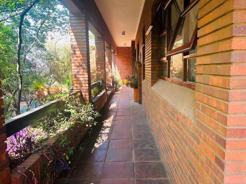 A spacious covered balcony featuring exposed brick pillars, tiled flooring, and integrated brick planter boxes overlooking the surrounding greenery.