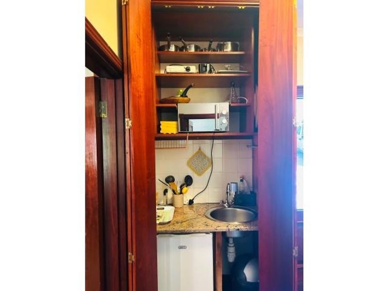 A compact scullery or kitchenette area featuring built-in wooden cabinetry, granite countertops, a stainless steel sink, and integrated microwave space.