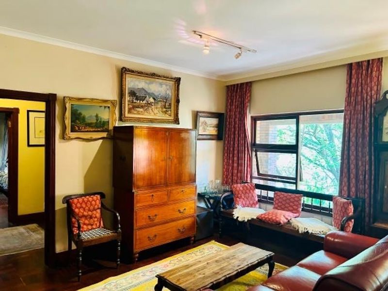 A traditional living room featuring warm parquet flooring, coved ceilings, and a large sliding window that provides natural light and garden views.