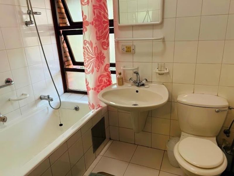 A functional bathroom featuring a bathtub with shower attachment, pedestal basin, and toilet, finished with white wall tiles and tiled flooring.