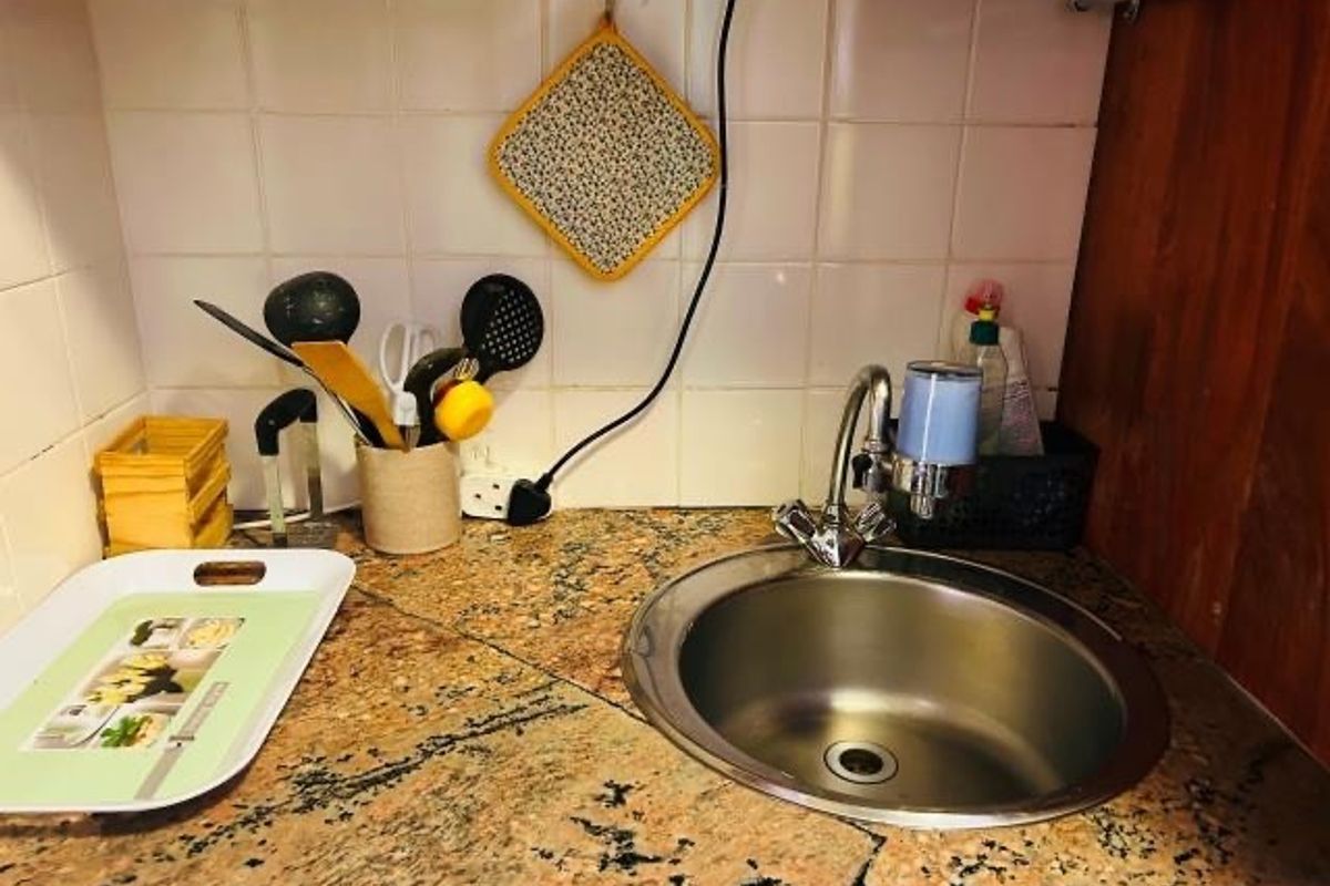 A compact kitchen prep area featuring a stainless steel sink, granite countertop, and tiled backsplash, showing signs of wear including a cracked countertop.