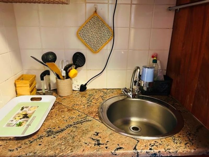 A compact kitchen prep area featuring a stainless steel sink, granite countertop, and tiled backsplash, showing signs of wear including a cracked countertop.