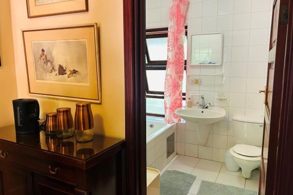 A functional bathroom featuring a pedestal washbasin, toilet, and bathtub with tiled finishes, accessible from the adjacent room.
