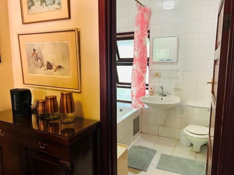 A functional bathroom featuring a pedestal washbasin, toilet, and bathtub with tiled finishes, accessible from the adjacent room.