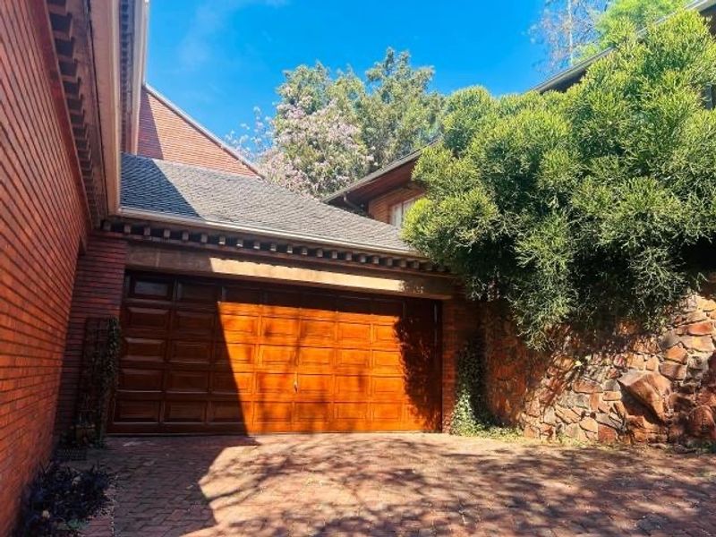 Exterior view of a residential property featuring a double wooden garage door, brick and stone facade, and a paved driveway.