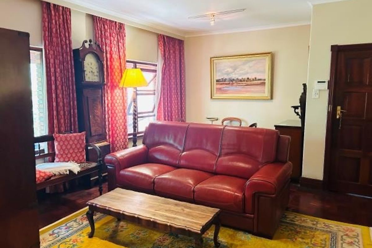 A traditional living room featuring hardwood flooring, coved ceilings, and a solid timber door, offering a classic and well-maintained living space.