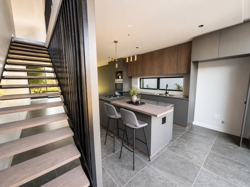 Modern open-plan kitchen featuring sleek cabinetry, a central island with breakfast bar, and a striking timber staircase with a contemporary metal balustrade.