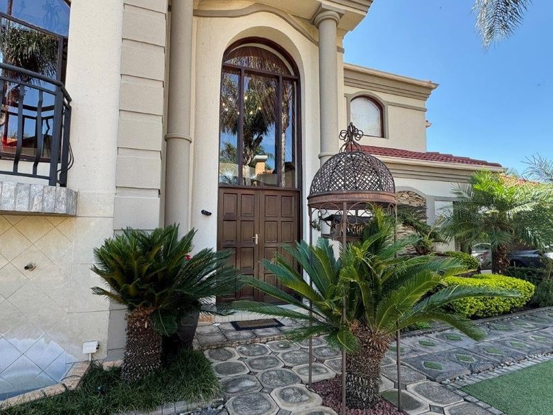 Grand front entrance featuring an arched double door, stone-paved walkway, and elegant architectural detailing on a well-maintained residential facade.