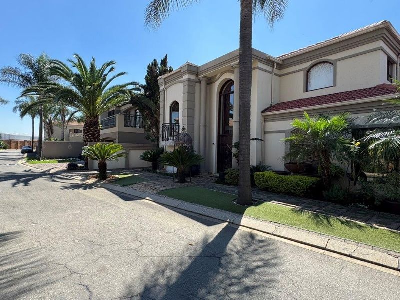 A well-maintained double-story residential property featuring a tiled roof, arched architectural details, a balcony, and a landscaped front garden.